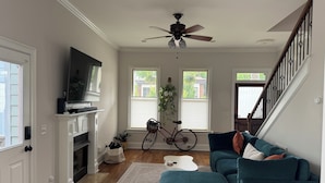 A living room with a fireplace, a television, a ceiling fan, a staircase, and a bicycle. - Bright & Airy 2-bed, 2.5-bath house in historic Germantown, Nashville (Nashville)
