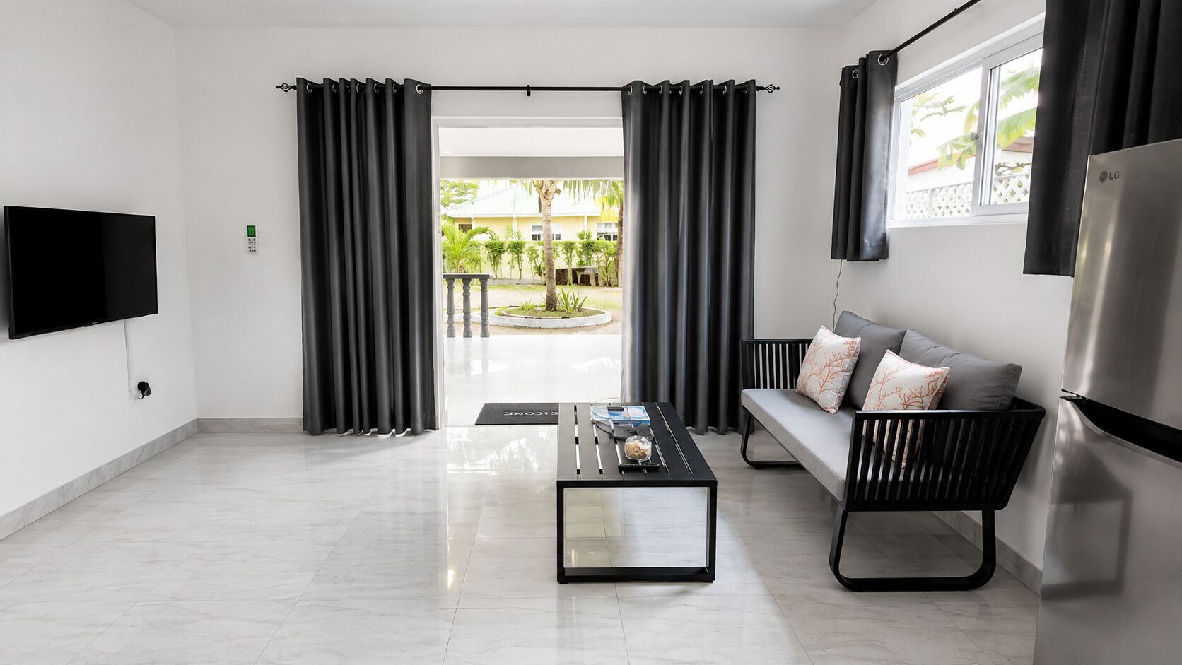 Una sala de estar moderna con una televisión de pantalla plana, un sofá con cojines, una mesa de centro y un ventanal con cortinas.