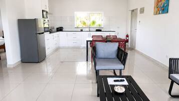 A spacious living area with a dining table, a sofa, and a kitchen in the background.