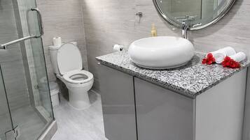 Un baño moderno con cabina de ducha de vidrio, inodoro blanco, espejo redondo y encimera de granito.