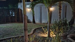 Ein nächtlicher Garten mit Palmen, einem Weg und einem Zierzaun.