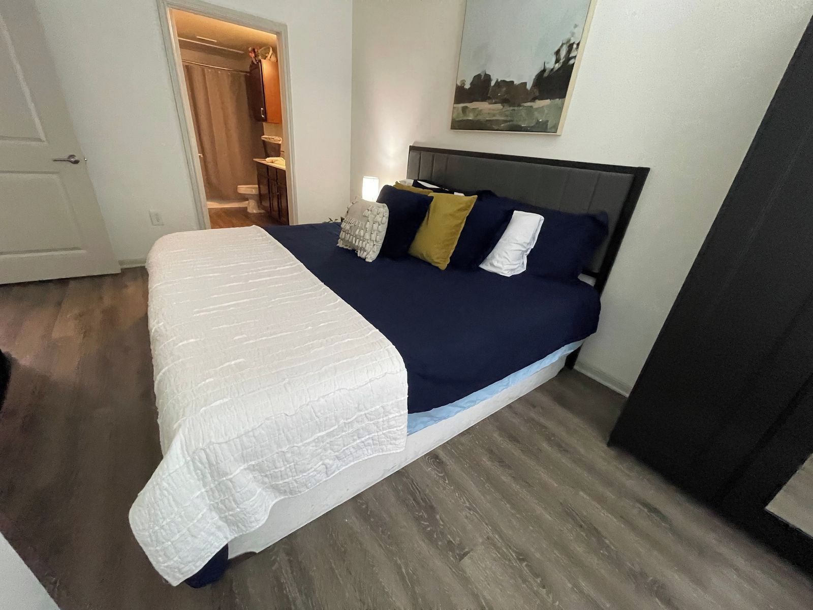 Une chambre à coucher avec un lit, une table de chevet, un tableau au mur et une porte donnant sur une salle de bain.