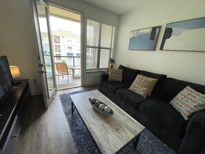 Una sala de estar con un sofá, una mesa de centro, un televisor y un ventanal corredero que da a un espacio exterior.