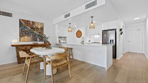 Una cocina moderna con armarios blancos, una isla central y un comedor con sillas de madera.