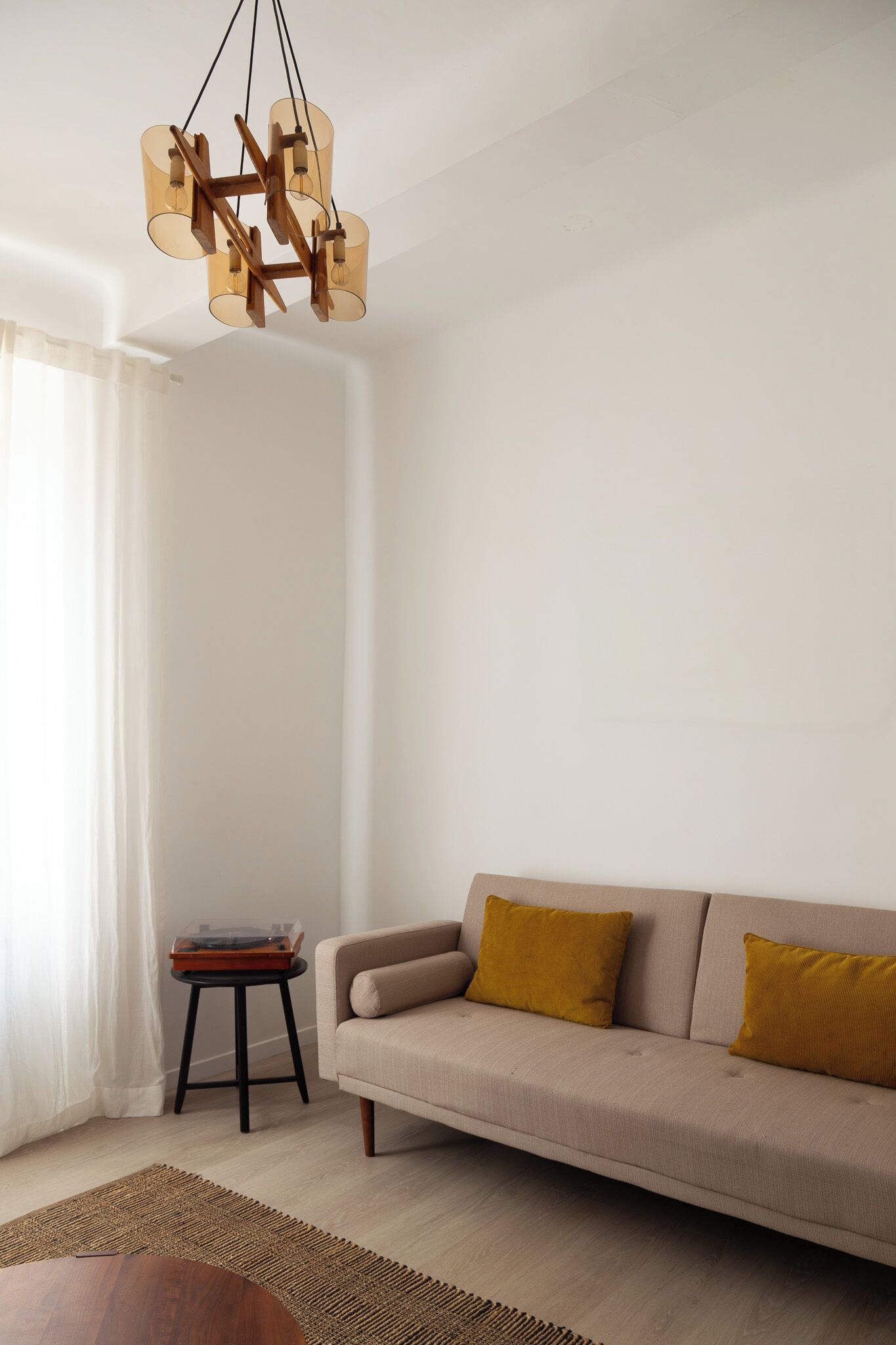 Een woonkamer met een beige bank, een houten salontafel en een bijzondere kroonluchter.