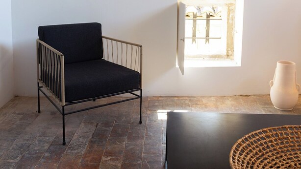 Une pièce avec un canapé noir, un vase blanc et une fenêtre donnant sur des arbres.