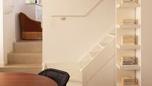 Un escalier avec une rampe blanche, une table en bois avec des chaises et une bibliothèque remplie de livres.