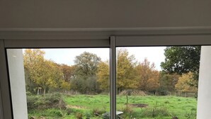 Blick durch eine Schiebetür auf einen Gartenbereich mit gepflasterter Terrasse, einem Schubkarren und einer Wasserflasche auf dem Boden.