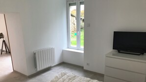 Ein Schlafzimmer mit einem Bett, einem Schminktisch, einem Heizkörper und einem Fenster mit Blick auf Grünflächen.