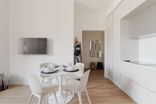 Un comedor moderno con una mesa redonda, sillas blancas y un televisor de pantalla plana montado en la pared.