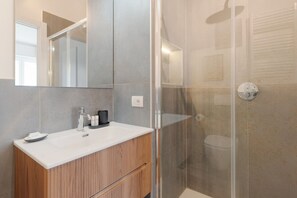 Un baño moderno con cabina de ducha de vidrio, tocador de madera y un espejo grande.