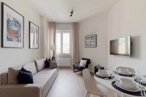 A modern living room with a sofa, a dining table set for four, and a flat-screen TV mounted on the wall. - GuestHost - Modern Apartment Lambrate Milano (Milan)