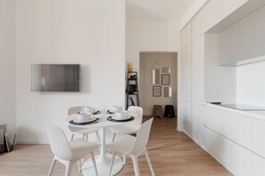 A modern dining area with a round table, white chairs, and a flat-screen TV mounted on the wall. - GuestHost - Modern Apartment Lambrate Milano (Milan)