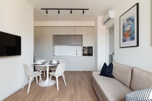 Una cocina moderna con armarios blancos, una mesa de comedor con sillas, un sofá y una obra de arte enmarcada en la pared.