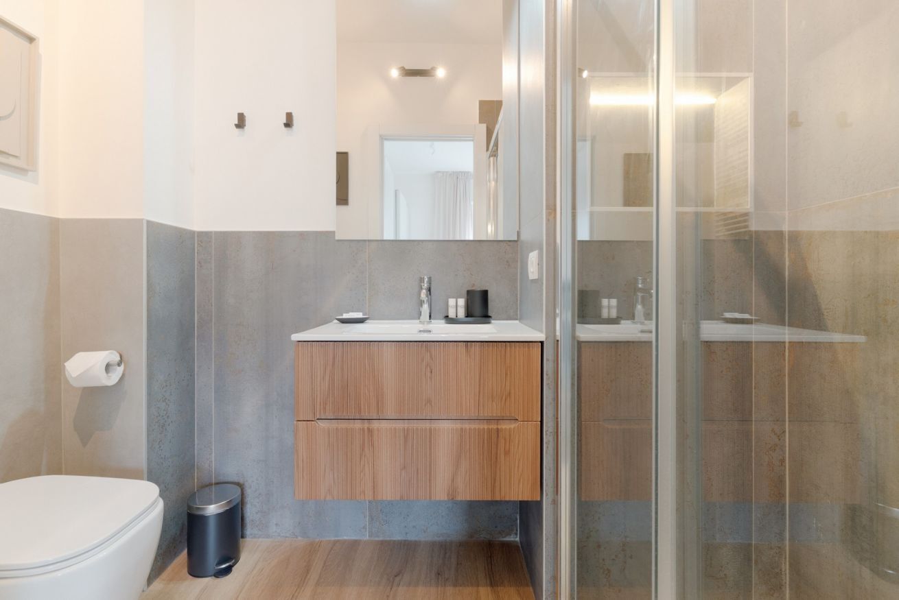 Ein modernes Badezimmer mit Toilette, Waschbecken, Waschtisch und einer Duschkabine aus Glas.