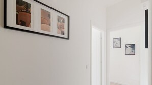 A hallway with framed abstract art on the wall, a white door, and a light wooden floor.