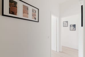 A hallway with framed abstract art on the wall, a white door, and a light wooden floor.