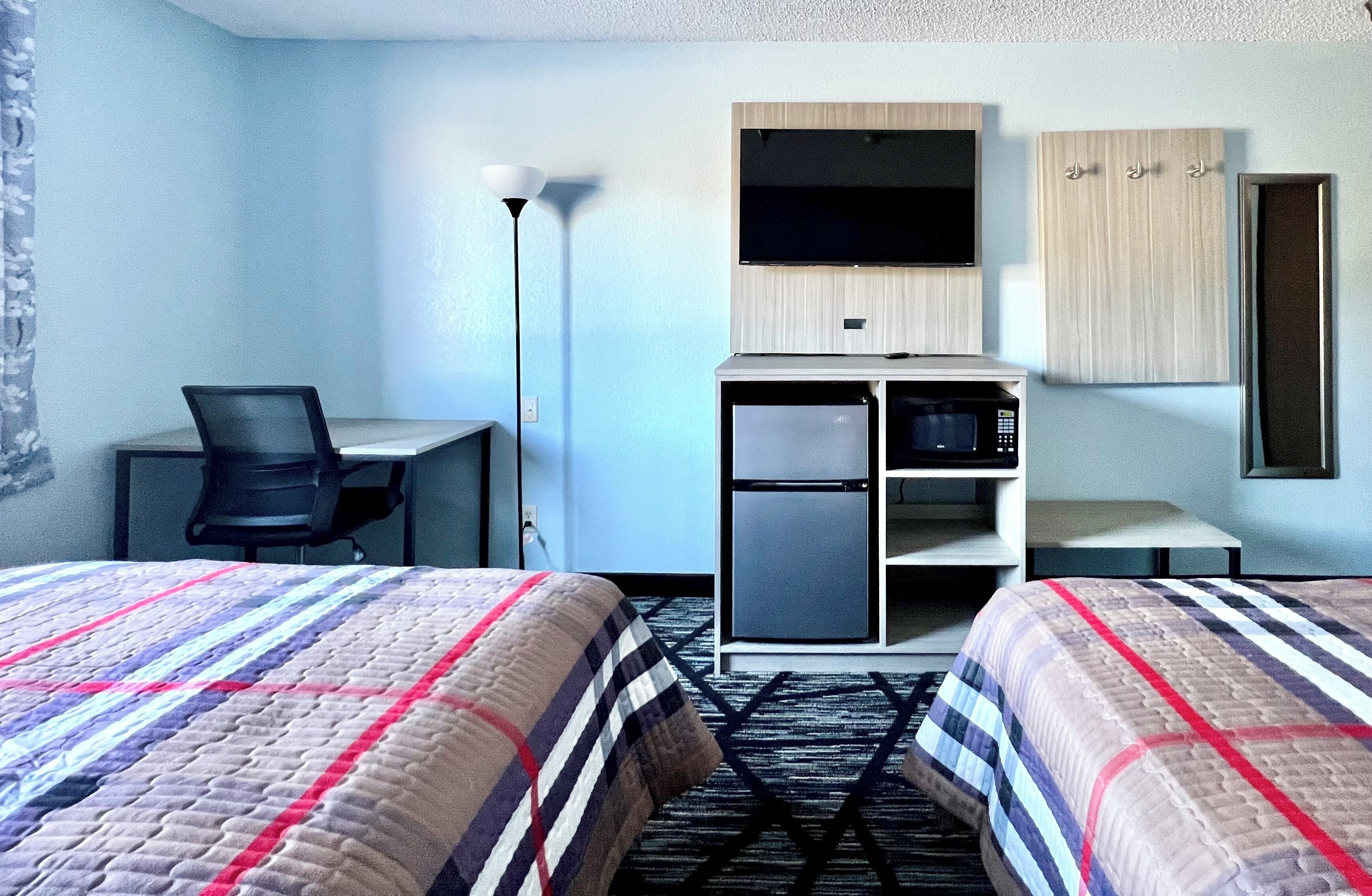 Une chambre d’hôtel avec deux lits, un bureau, une chaise, une télévision, un four à micro-ondes et une armoire.