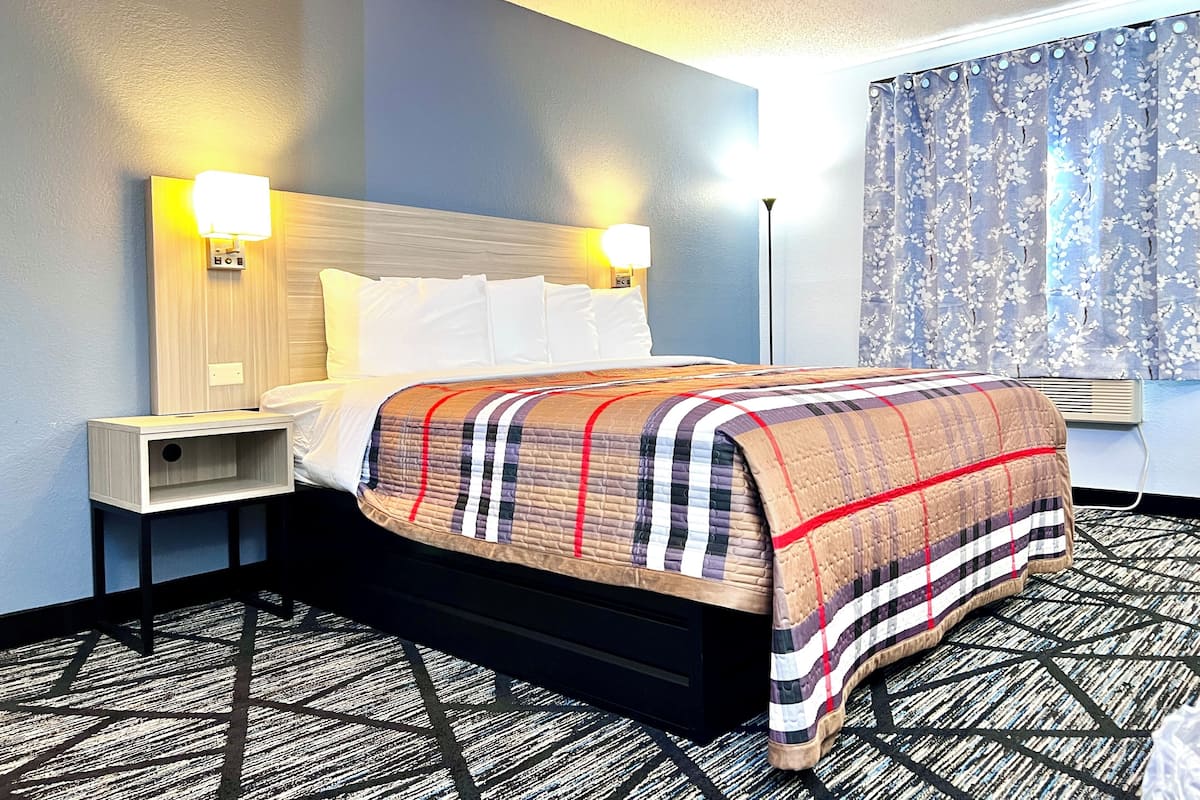 Une chambre d’hôtel avec un lit, des tables de chevet, une tête de lit, une fenêtre avec des rideaux et une moquette à motifs.