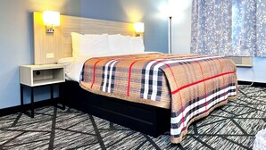 Habitación de hotel con cama, mesitas de noche, cabecera, ventana con cortinas y alfombra estampada.