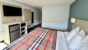 Una habitación de hotel con cama, escritorio con computadora, televisor de pantalla plana y armario.