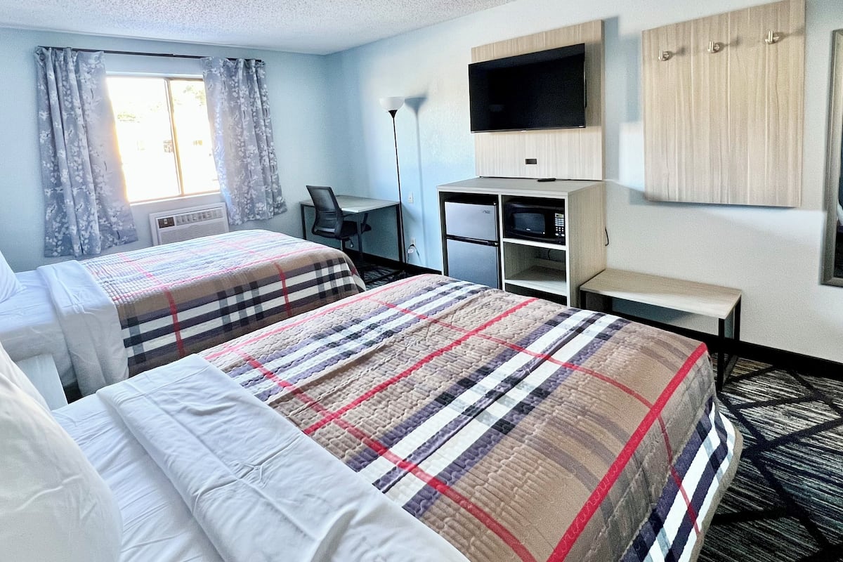 Une chambre d’hôtel avec deux lits, un bureau, une chaise, une télévision, une armoire et une fenêtre avec des rideaux.