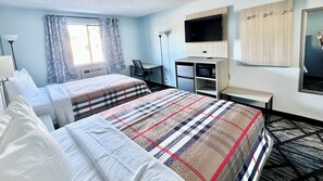 Quarto de hotel com duas camas, uma escrivaninha, uma cadeira, uma televisão, um guarda-roupa e uma janela com cortinas.