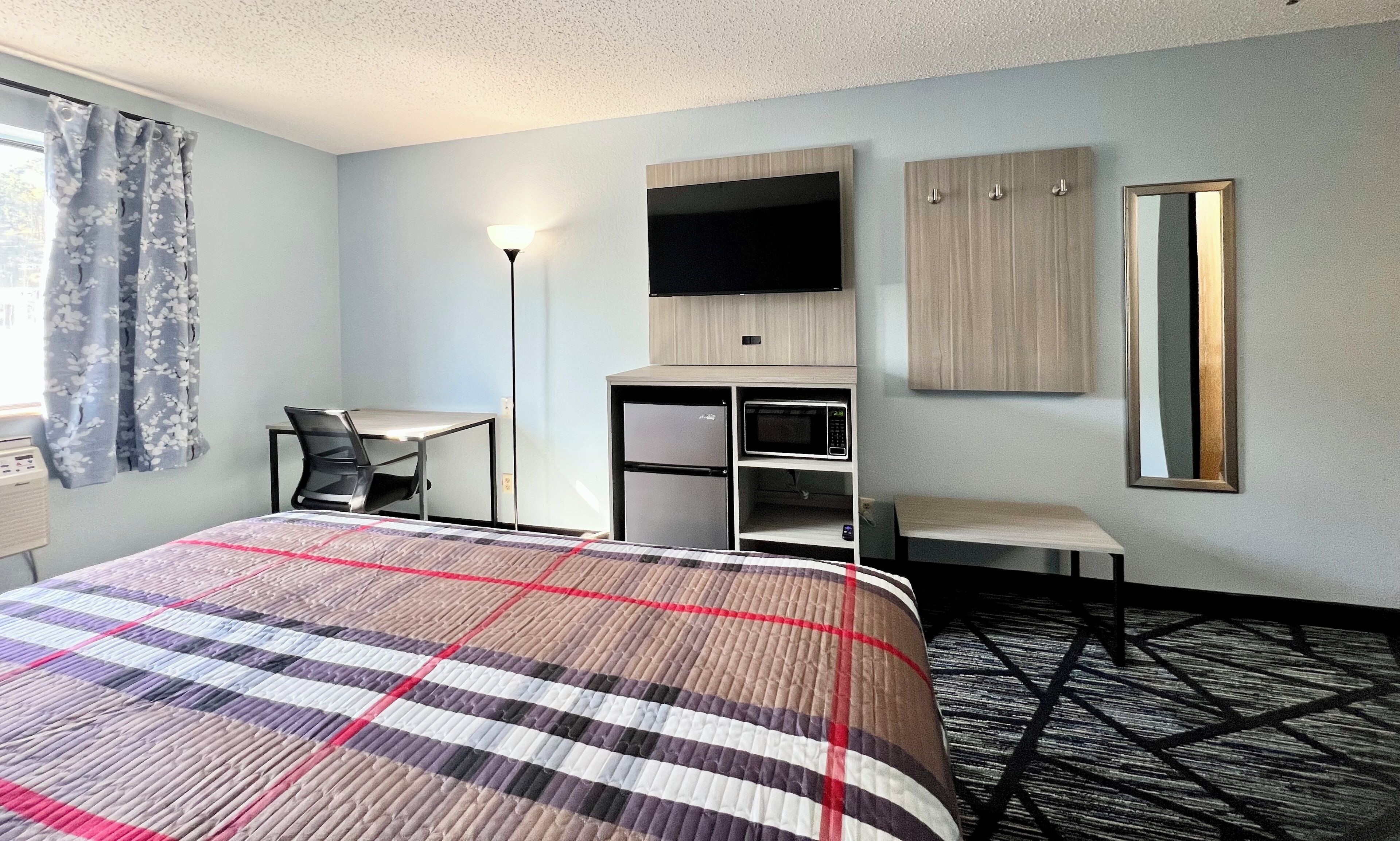 Hotelkamer met een bed, bureau, stoel, flatscreen-tv, garderobe en spiegel.