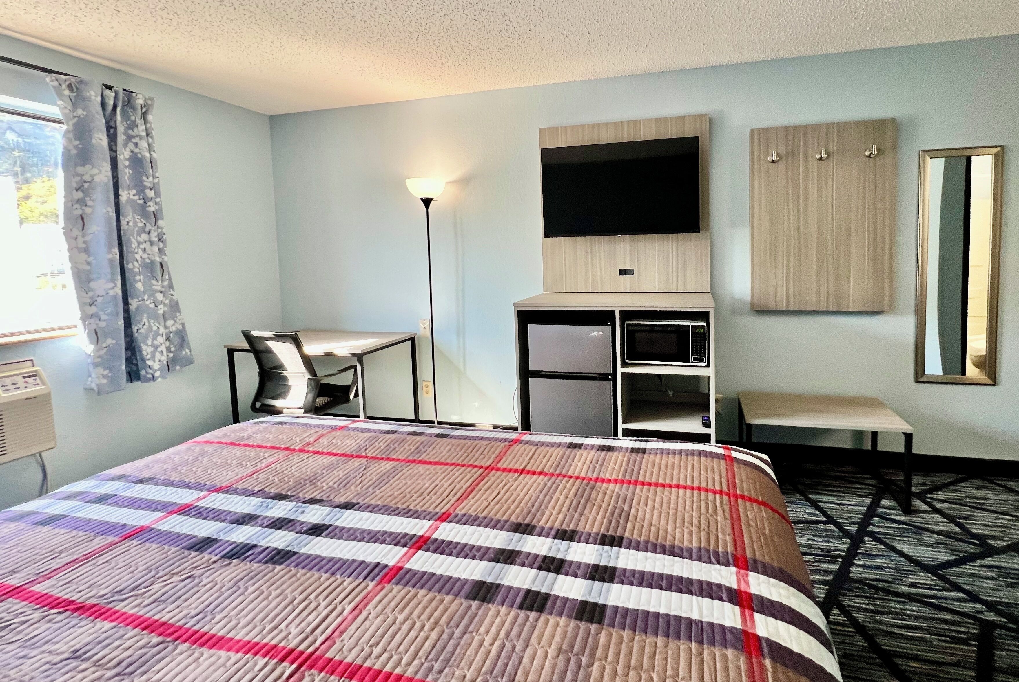 A hotel room with a bed, a desk, a chair, a TV, a wardrobe, and a mirror.