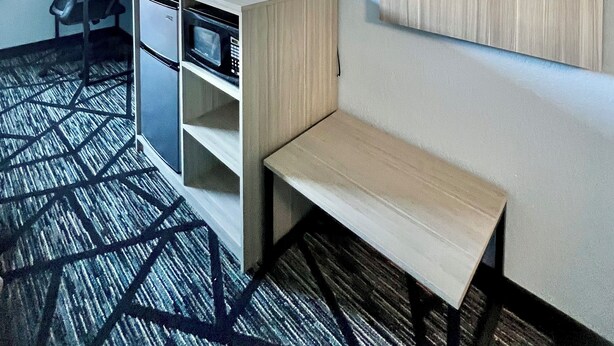 Habitación de hotel con escritorio, silla, televisor, armario y alfombra estampada.