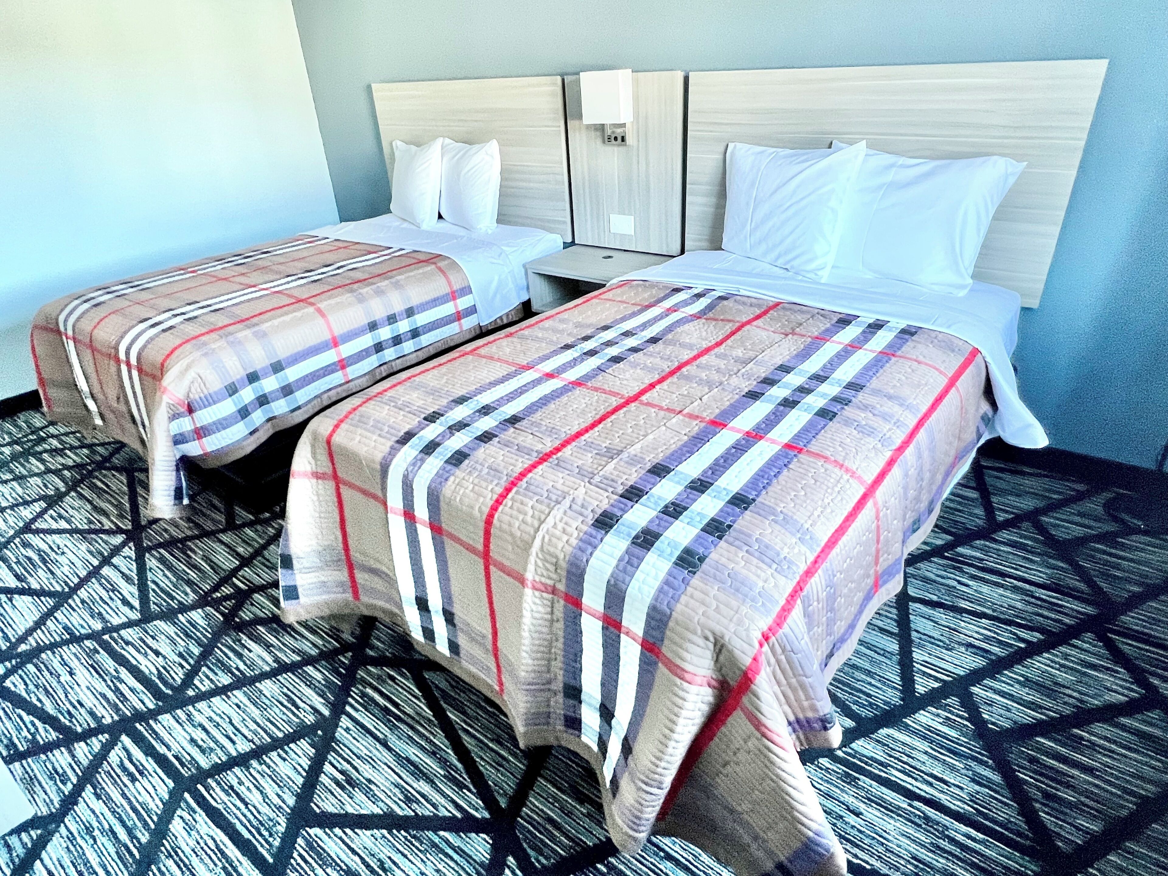 Two beds with plaid bedding, a headboard, and a geometric-patterned carpet.