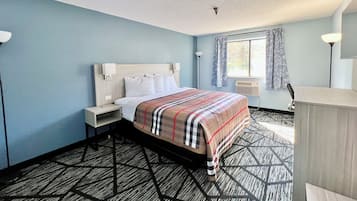 Une chambre d’hôtel comprenant un lit, une table de chevet, une lampe, une fenêtre avec des rideaux et un radiateur.