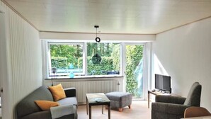 Ett modernt vardagsrum med en soffa, en pall och en fåtölj, ett litet bord och en tv som står på ett tv-bord.