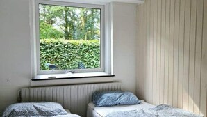 A bedroom with two beds, a window with a view of greenery, and a radiator under the window. - Sea sun (Nørre Nebel)