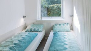 Une petite pièce lumineuse, avec deux lits simples, une fenêtre donnant sur un espace verdoyant et un radiateur en dessous.