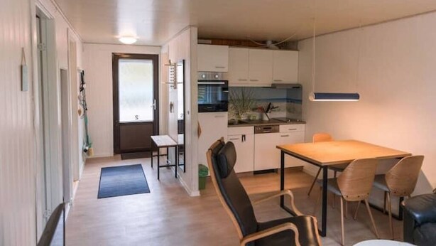 Une cuisine compacte avec des meubles blancs, un coin repas comprenant une table et des chaises, et un petit espace détente avec un banc.