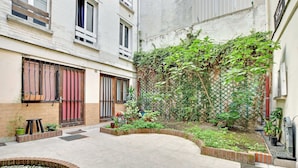 Un cortile con pavimento piastrellato, una piccola fontana, piante in vaso e un cordone di mattoni.