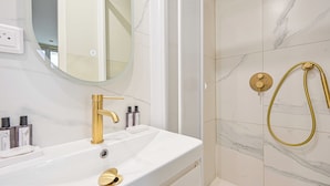 Un bagno con un lavandino bianco, un rubinetto dorato e una doccia con soffione dorato.