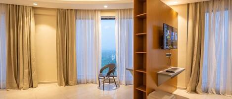 Ein modernes Hotelzimmer mit gewölbter Decke, einem an einer Holzwand montierten Fernseher, einem Sessel und Blick auf die Stadt durch große Fenster.