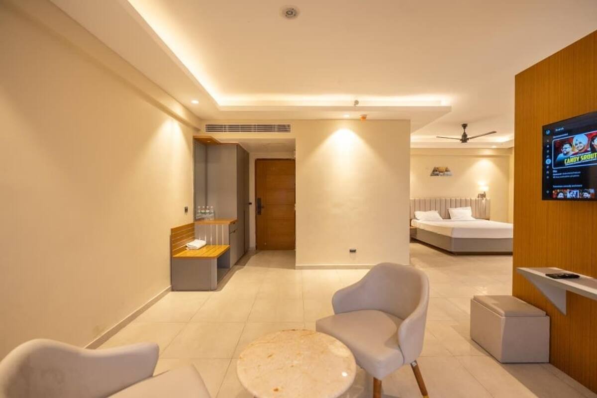 Una habitación de hotel moderna con una cama, una zona de estar con una mesa redonda, un televisor montado en la pared y una kitchenette.
