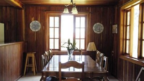 A wooden-paneled dining room with a large table and chairs, two wall-mounted lamps, and a window with a view. - Cabin in Cerro Punta  6BR, Fireplace, Hiking (Cerro Punta)