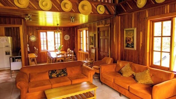 A wooden interior with a sofa, dining table, and chairs. - Cabin in Cerro Punta  6BR, Fireplace, Hiking (Cerro Punta)