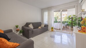Una sala moderna con un sofá gris, una mesita redonda y un balcón con vistas al exterior.