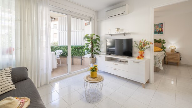 Una sala de estar moderna con un sofá, televisión, armarios blancos y una pequeña mesa redonda con una planta.