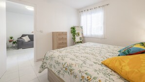 Un dormitorio con cama, cómoda, espejo, ventana con persianas y puerta que da a otra habitación.