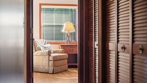 Una habitación con un sillón color crema, una mesita de noche de madera y una lámpara.