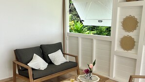 Een kamer met een houten bank, een houten bijzettafeltje met een vaas en glazen, en uitzicht op groen.