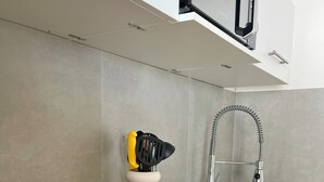 Een keuken met een houten aanrecht, een roestvrijstalen spoelbak en een magnetron erboven. Op het aanrecht ligt een brood, twee witte mokken en een citroen.