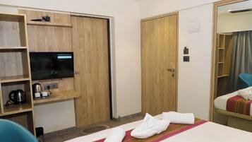 A hotel room with a bed, a TV, a desk with a kettle, and a wardrobe.