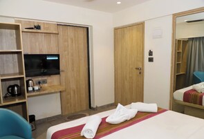 A hotel room with a bed, a TV, a desk with a kettle, and a wardrobe.
